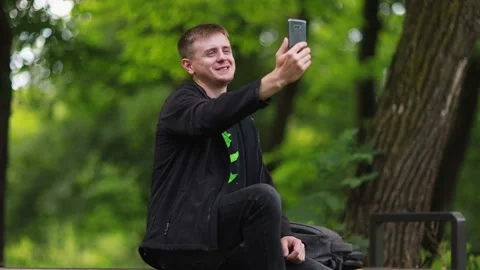 A young guy is having fun chatting with his friends via video call in the park. Stock Footage 201824473