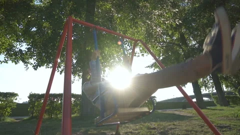 Young guy having fun swinging on swing on a playground at sunset time Stock Footage 106626374