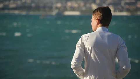 A young guy with his back to the camera , looking at the sea, straightening his  Vidéo 114139857