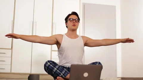 Young guy in home clothes lazily doing yoga on a gray.man spreading his arms 動画素材 259489255