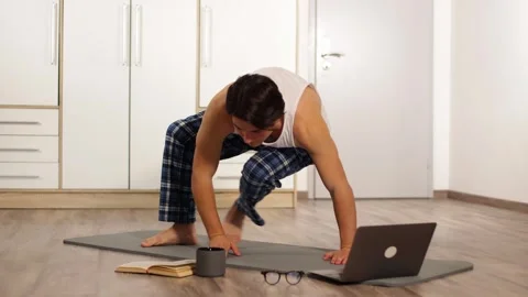 Young guy in home lazily doing yoga on gray carpet.repeats pose and falls funny Vidéo 253826672