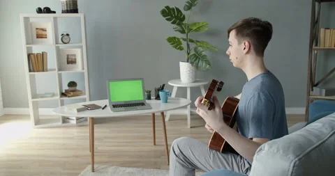A young guy at home is learning to play the guitar using the Internet.Laptop Stock Footage 132043771