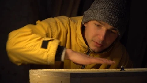 Young guy joiner blows wood shavings off the work surface Stock Footage 125859341