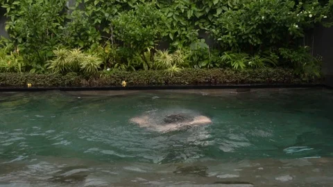 Young guy jumps out of the water of pool with his arms outstretched. Stock Footage 104348514