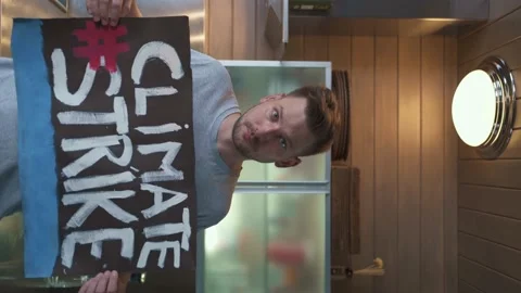 A young guy in the kitchen at home holds a poster that says "Climate Strike" Video stock 151534852