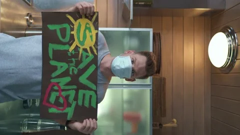 A young guy in the kitchen at home holds a poster that says "Save the Planet" Stock Footage 151534965