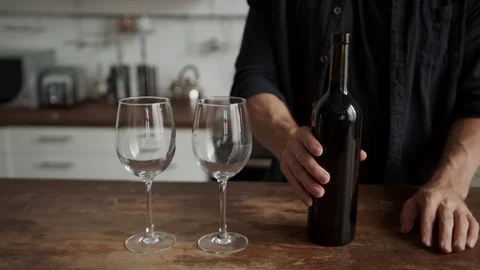 A young guy in the kitchen pours wine into glasses. romantic date. prepare for a 스톡 동영상 117431723