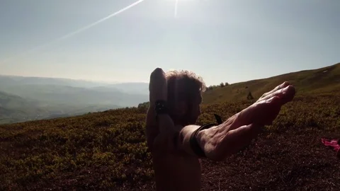 A young guy kneads his hands behind his back from behind, in the mountains, yoga Stock Footage 77786428