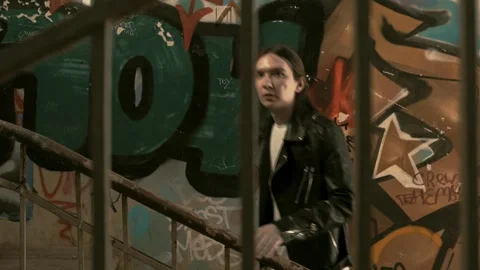 Young guy in a leather jacket with long hair walks up the stairs Stock Footage 287914935