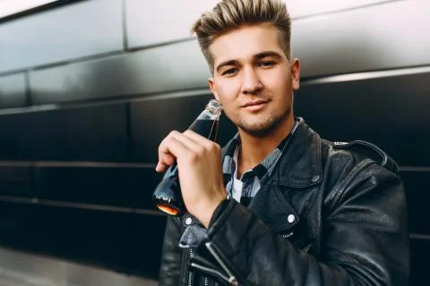 A young guy in a leather jacket, standing near a black wall in the city with  Stock Photos