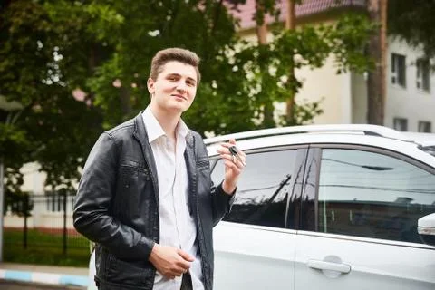 A young guy in a leather jacket is standing near his car. Stock Photos