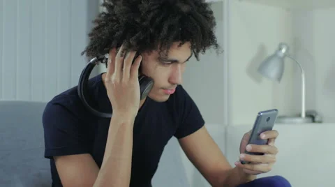 Young guy listens to music in one earphone and thumbs through news in phone Stock Footage 58587159
