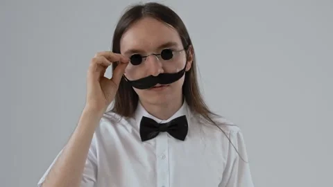 Young guy with long hair with a false moustache wearing a hat and glasses. Stock Footage 287915601