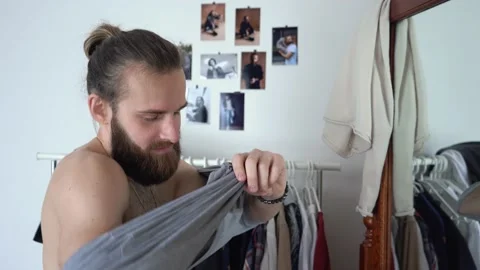 Young guy with long hair is looking into the mirror Putting together an outfit Stock Footage 147896893