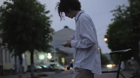 Young Guy With Long Hair Using Smart Phone Navigator In City With Bike Evening Stock Footage 62809166