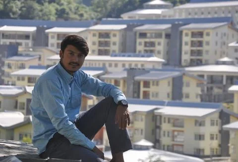 A young guy looking at camera sitting outside with buildings in background Foto stock