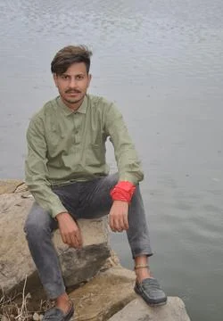 A young guy looking at camera while sitting on stone next to the lake Stock Photos