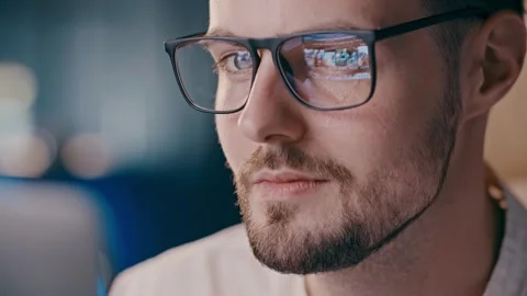 Young guy looking at screen with content in glasses reflection. Serious Stock Footage 257800329