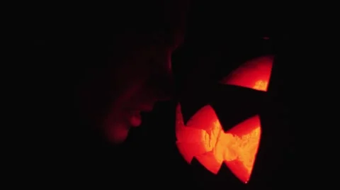 Young guy looks on burning candle inside of carved pumpkin jack o lantern face Stock Footage 68176147
