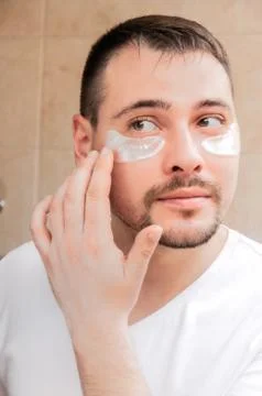 A young guy looks at himself in a mirror with silver patches under his eyes.  Stock Photos
