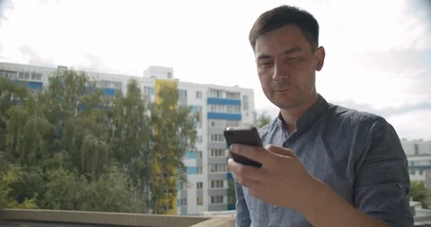 Young guy looks into the phone, in the background yard Video stock 113284637