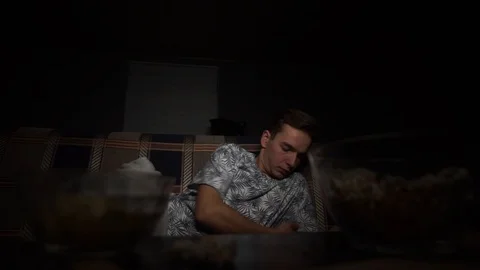 The young guy is lying on the bed and watching TV, looking for a remote Stock Footage 126093374