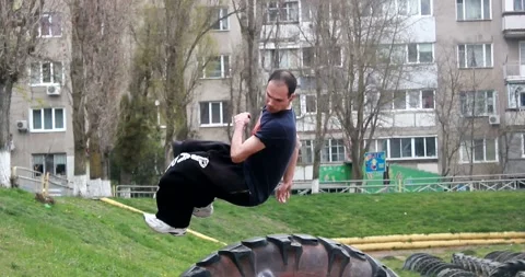 A young guy makes an acrobatic turn through a large tire in parkour style Stock Footage 265051285