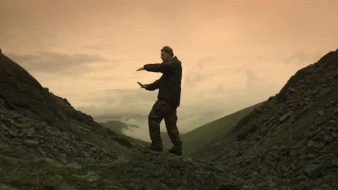 Young guy makes smooth movements with his hands standing on a mountain crossing Stock Footage 164558290