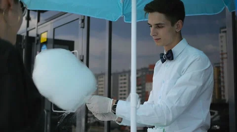 Young guy making cotton candy on a special machine, it wears bow tie, behind him Stock Footage 64042343