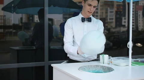 Young guy making cotton candy on a special machine, it wears bow tie, behind him Stock Footage 64043092