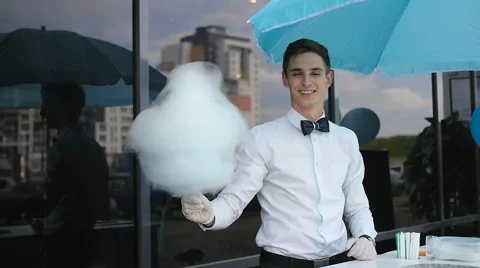 Young guy making cotton candy on a special machine, it wears bow tie, behind him Stock Footage 64043159