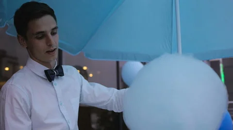 Young guy making cotton candy on a special machine, it wears bow tie, behind him Stock Footage 64043307