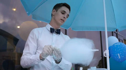 Young guy making cotton candy on a special machine, it wears bow tie, behind him Stock Footage 64044027