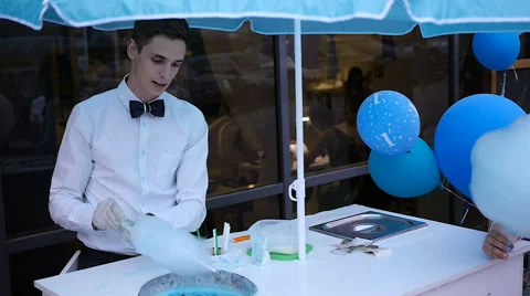 Young guy making cotton candy on a special machine, it wears bow tie, behind him Stock Footage 64044256