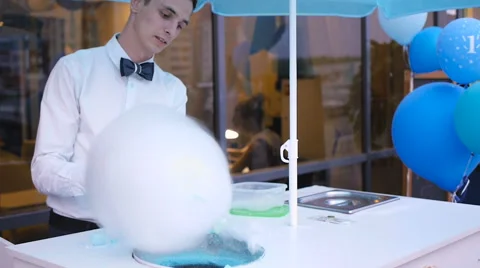 Young guy making cotton candy on a special machine, it wears bow tie, behind him Stock Footage 64044435