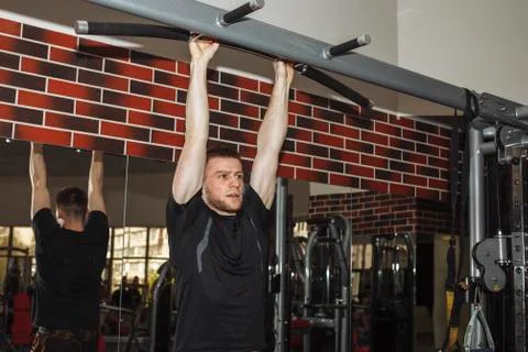 A young guy, a man pulls himself up on a crossbar in the gym. Performs weight Stock Photos