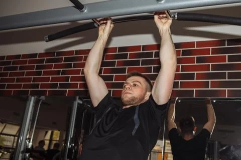 A young guy, a man pulls himself up on a crossbar in the gym. Performs weight Stock Photos
