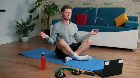 Young guy meditating in lotus pose on exercise mat at home. Stock Footage 144615442