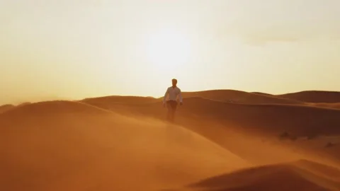Young guy, a model in a white shirt, walks on the sands in the desert Stock Footage 305723013