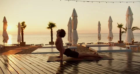 A young guy with a naked torso does yoga and gets up on his hands at sunrise Stock Footage 249606822