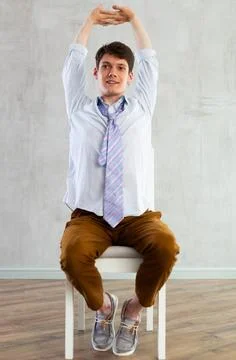 Young guy office worker doing exercises on chair Stock Photos
