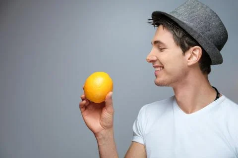 A young guy with an orange in his hand wearing a hat Stock Photos
