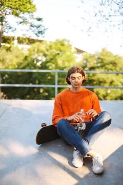Young guy in orange pullover with skateboard holding bottle of water in hand Stock Photos