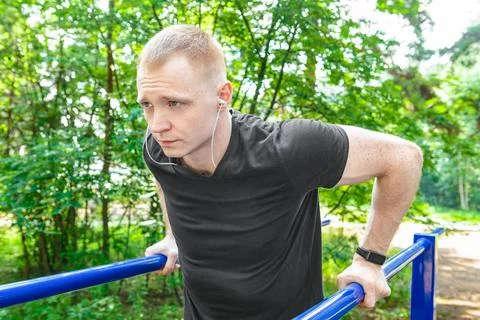 A young guy performs an exercise on the uneven bars. Stock Photos