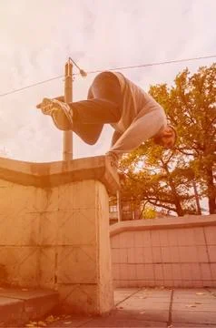 A young guy performs a jump through the concrete parapet. The athlete practic Stock Photos