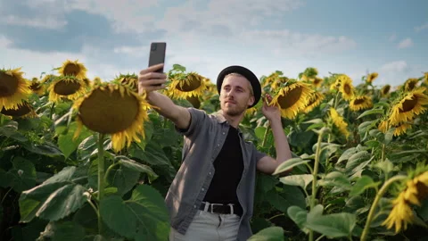 Young guy with, pierced in a sunflower field takes a selfie on the phone camera Video stock 162963242