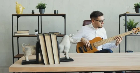 Young guy is playing on guitar and enjoying it sitting in office during break. Stock Footage 120833890