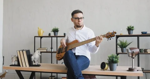 Young guy playing guitar enjoying it sitting on office table, camera in motion. Vídeo Stock 120834719
