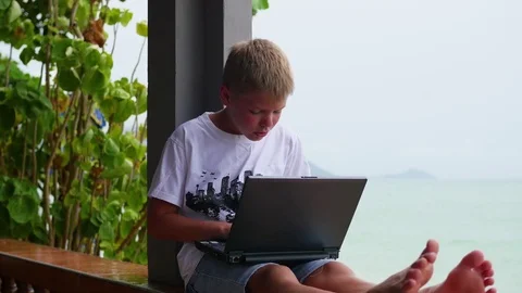 Young guy playing on a laptop, sitting on the terrace. Near the sea and the Video stock 75791415