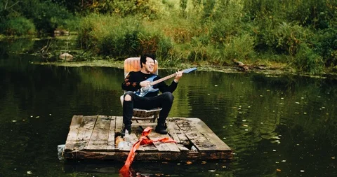 A young guy plays and sings sitting on a raft in the middle of a pond. Stock Footage 114520389